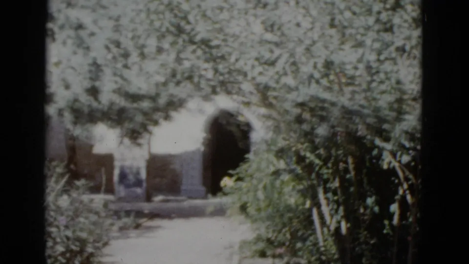 1952 8mm home-movie frame showing a rounded stone arch set in a masonry wall, surrounded by lush foliage, likely in New Orleans.