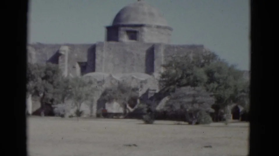Exterior of a mission-style building with dome and adobe walls across dry open ground — 8mm color reversal film, likely American Southwest, 1952.
