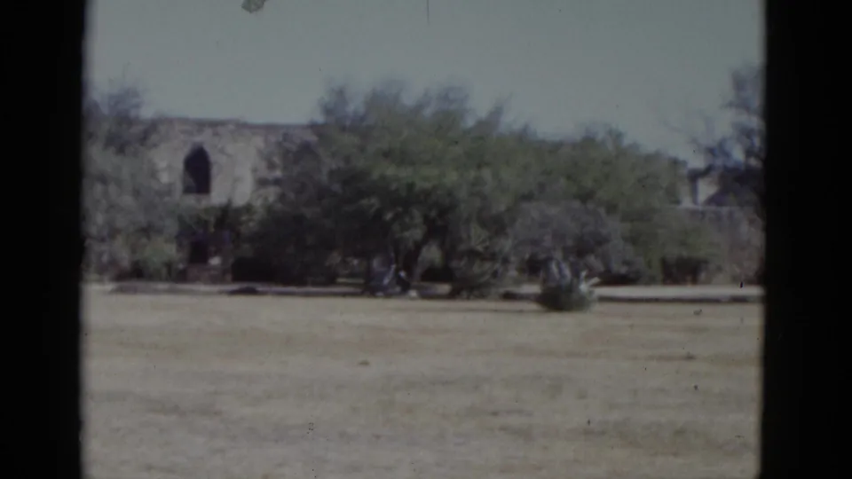 8mm home movie circa 1952 showing stone mission-style walls and a secondary stone structure behind trees across an arid field.