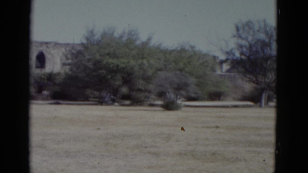 1952 8mm home movie establishing shot: arid open field, sparse trees, and a stone structure with an arched window, possibly at a Southwest US historic site.