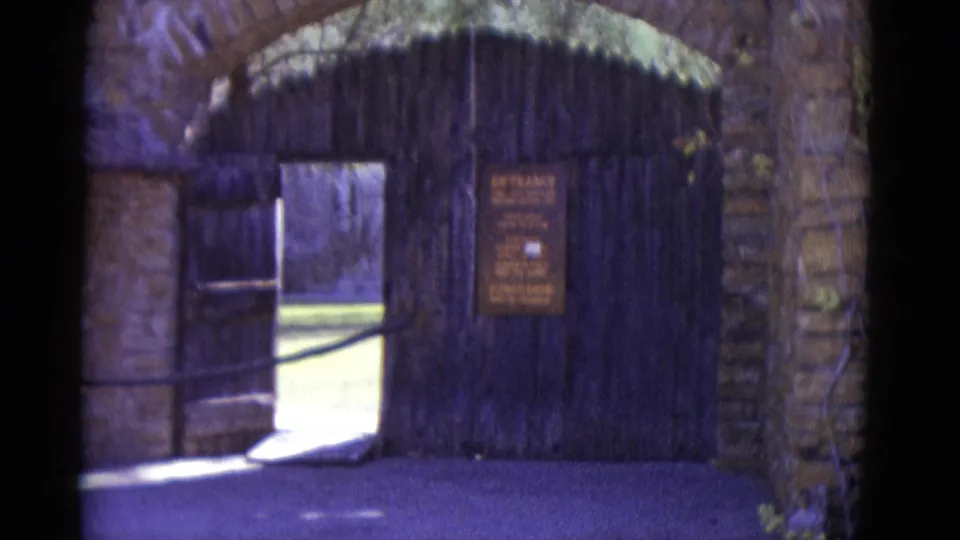 Wooden arched entrance gate with stone surround and a partially legible hand-painted entrance sign at an outdoor public venue, New Orleans area, 1952.