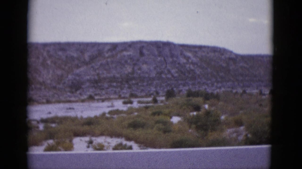 1952 8mm home-movie frame showing a flat-topped rocky mesa over Texas desert scrubland, filmed from a moving vehicle.