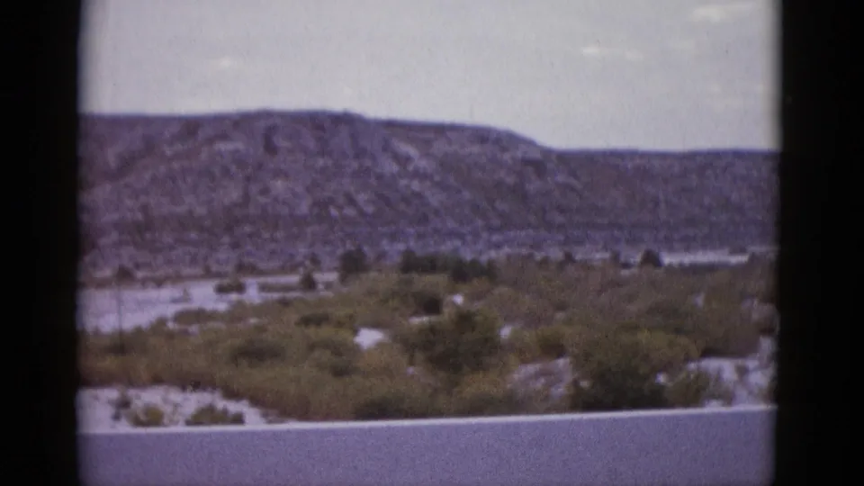 Mid-clip 8mm frame from 1952 Texas road trip showing rocky ridge and desert scrub under a pale overcast sky.