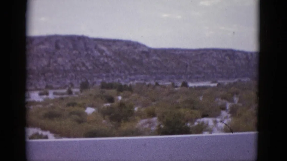 Final frame of 1952 8mm Texas road-trip clip showing the rocky mesa and desert scrubland as the vehicle continues past.