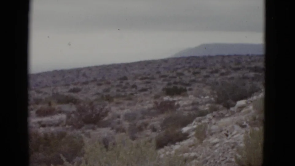 Continuation of 1952 Texas 8mm road-trip footage showing rocky arid terrain, scrub vegetation, and a mountain silhouette under gray overcast sky.