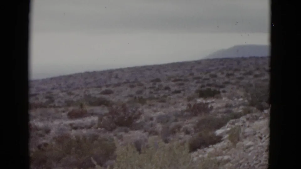 8mm footage from 1952 Texas showing a widened desert vista after an apparent pan, with a mountain silhouette prominent against the overcast sky and scrubland below.