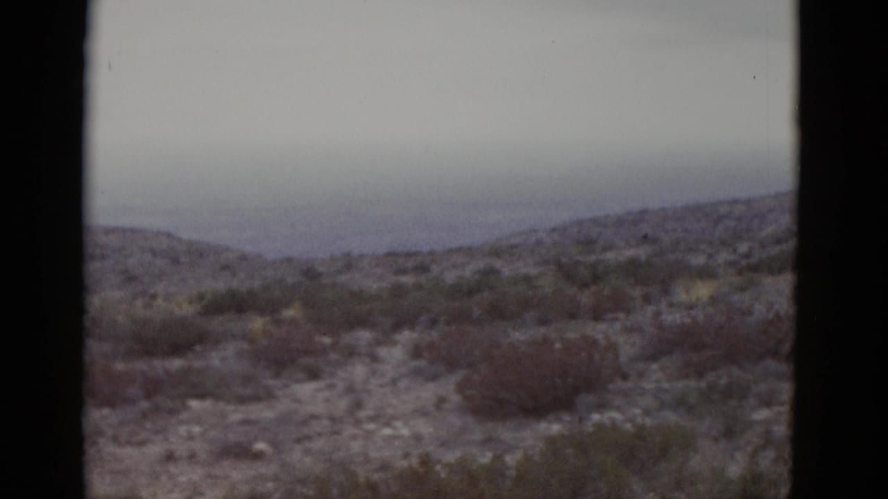 Desert hills with sparse scrub brush under an overcast sky, 8mm film.