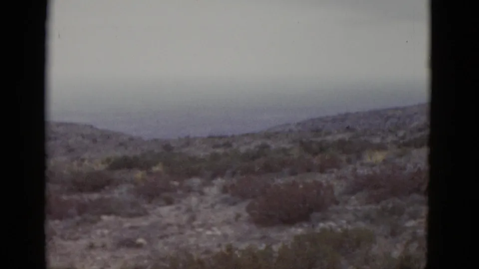 1952 Texas desert landscape on 8mm — rolling scrub-covered hills and a heavy grey sky with muted color palette.
