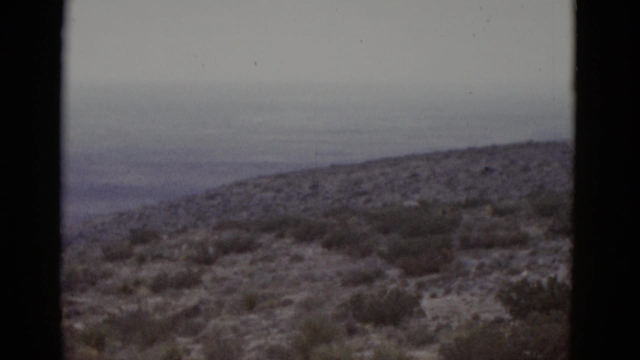 Desert scrub brush and hills under a flat overcast sky, camera panning right.