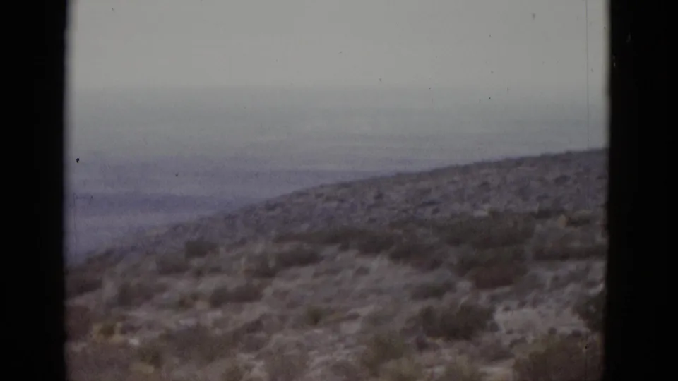 1952 Texas desert on 8mm — wide valley basin with a rounded hill and layered receding ridgelines under grey overcast.