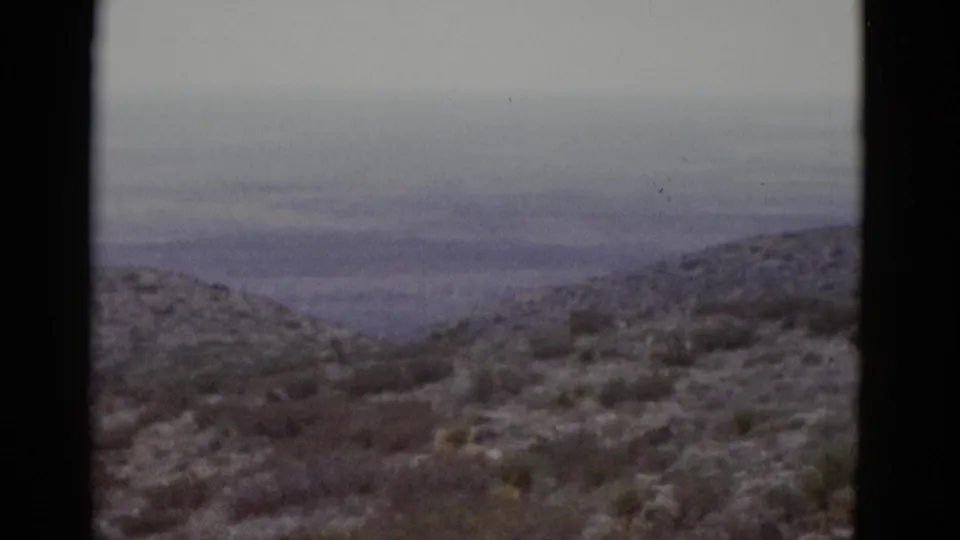 1952 Texas desert on 8mm — layered ridgelines recede into a hazy blue-grey overcast horizon with scrub brush foreground.