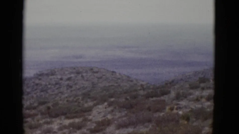 Wider view of Utah desert landscape on 8mm film circa 1952, showing an arid scrub-covered hill and a flat valley basin stretching to the horizon.
