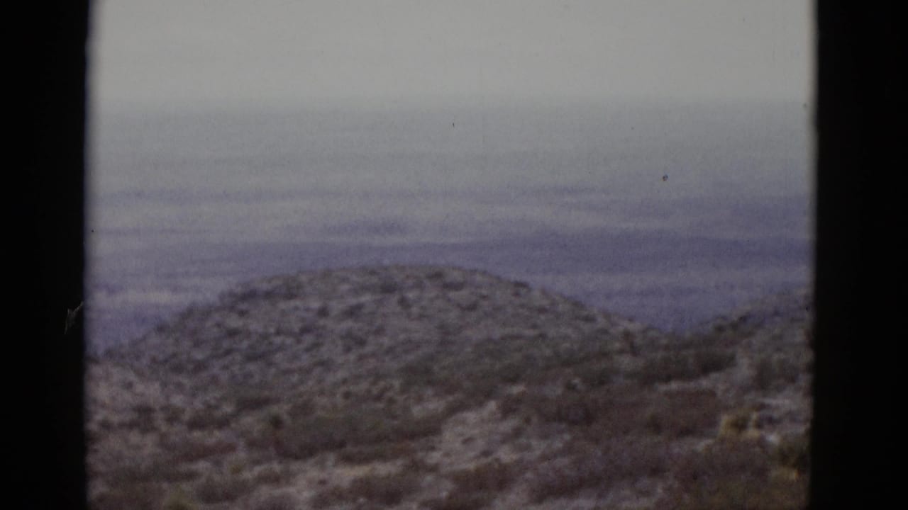 16mm film frame showing a rounded hill with light snow and sparse scrub brush, under an overcast sky, from a 1952 Utah landscape pan.