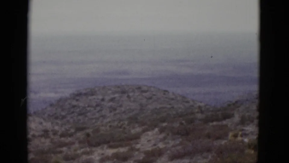 16mm film frame showing a rounded hill with light snow and sparse scrub brush, under an overcast sky, from a 1952 Utah landscape pan.