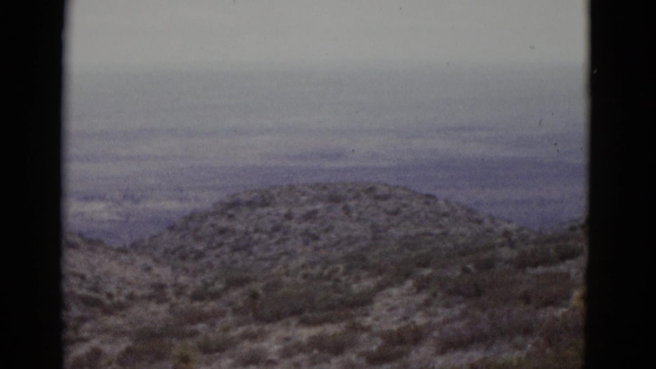 Mid-pan 16mm frame from 1952 Utah showing snow-dusted hills with sparse scrub vegetation and a layered blue-gray overcast sky.