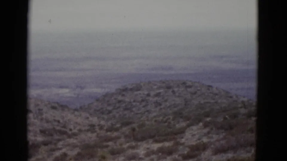 16mm frame from 1952 Utah pan showing snow-dusted hills in foreground and a hazy distant valley floor beneath a flat overcast sky.