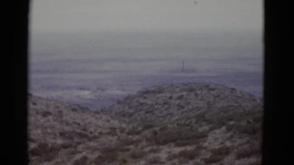 Closing 16mm frame from 1952 Utah pan; snow-dusted scrub hills and distant hazy basin with a faint unidentified vertical element at far right edge.