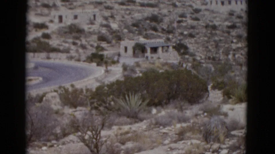 Small stone structure with arched colonnade on rocky Utah desert hillside, winding road below, agave plants visible, circa 1952 8mm footage.