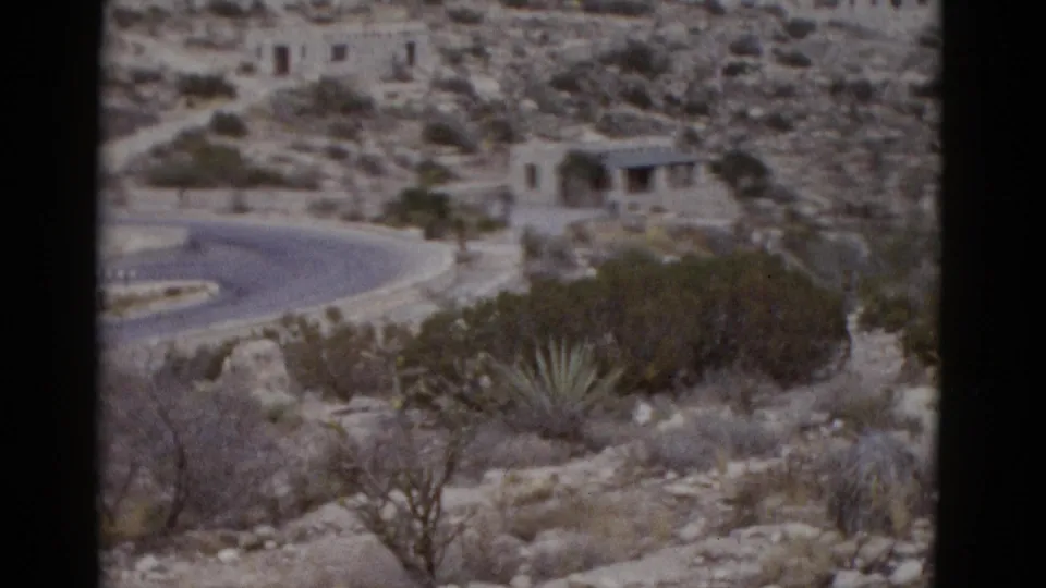 Winding road through arid Utah desert with stone structure, agave plants, and rocky hillside in 8mm footage, circa 1952.