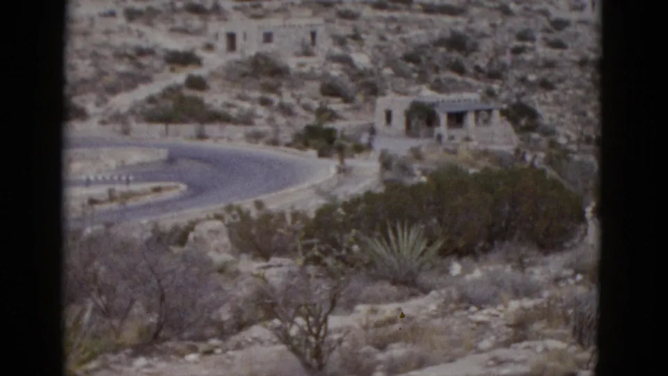 Stone building with arched facade on rocky Utah desert hillside, winding road foreground, agave and scrub brush, circa 1952 8mm.