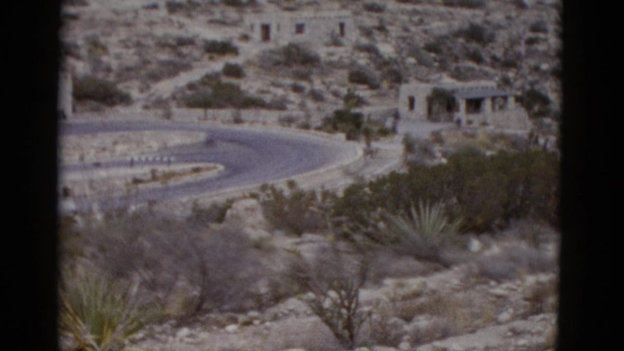 Desert hillside with switchback road and stone structure visible above, agave plants in foreground
