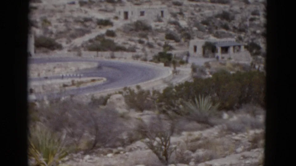 Early pan frame of 1950s 8mm footage showing a switchback desert road and a stone structure on the upper slope, possibly Utah, with agave in foreground