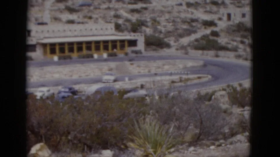 Final pan frame of 1950s 8mm clip showing stone roadside building with yellow arcade, several mid-century automobiles, and desert scrub in what may be Utah