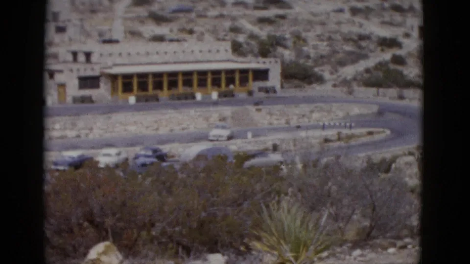 Elevated view of a low-profile stone-and-beam building in an arid Utah setting, circa 1952, with 1950s automobiles parked below and yucca plants in the foreground.