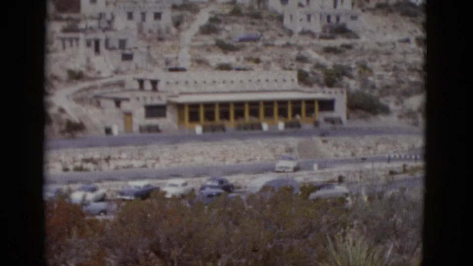 Wider angle showing the full extent of a stone-and-beam institutional building in Utah desert, circa 1952, with curved access road, parked cars, and rocky terrain.