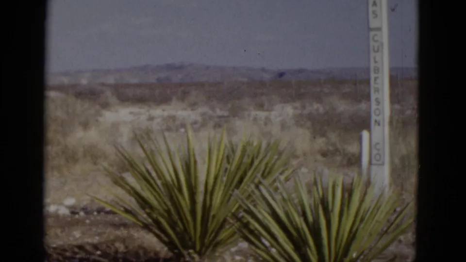 Foreground yucca plant beside sign post reading 'CULBERSON CO', wide desert plain and mountain range beyond; American Southwest, circa 1952 8mm footage.