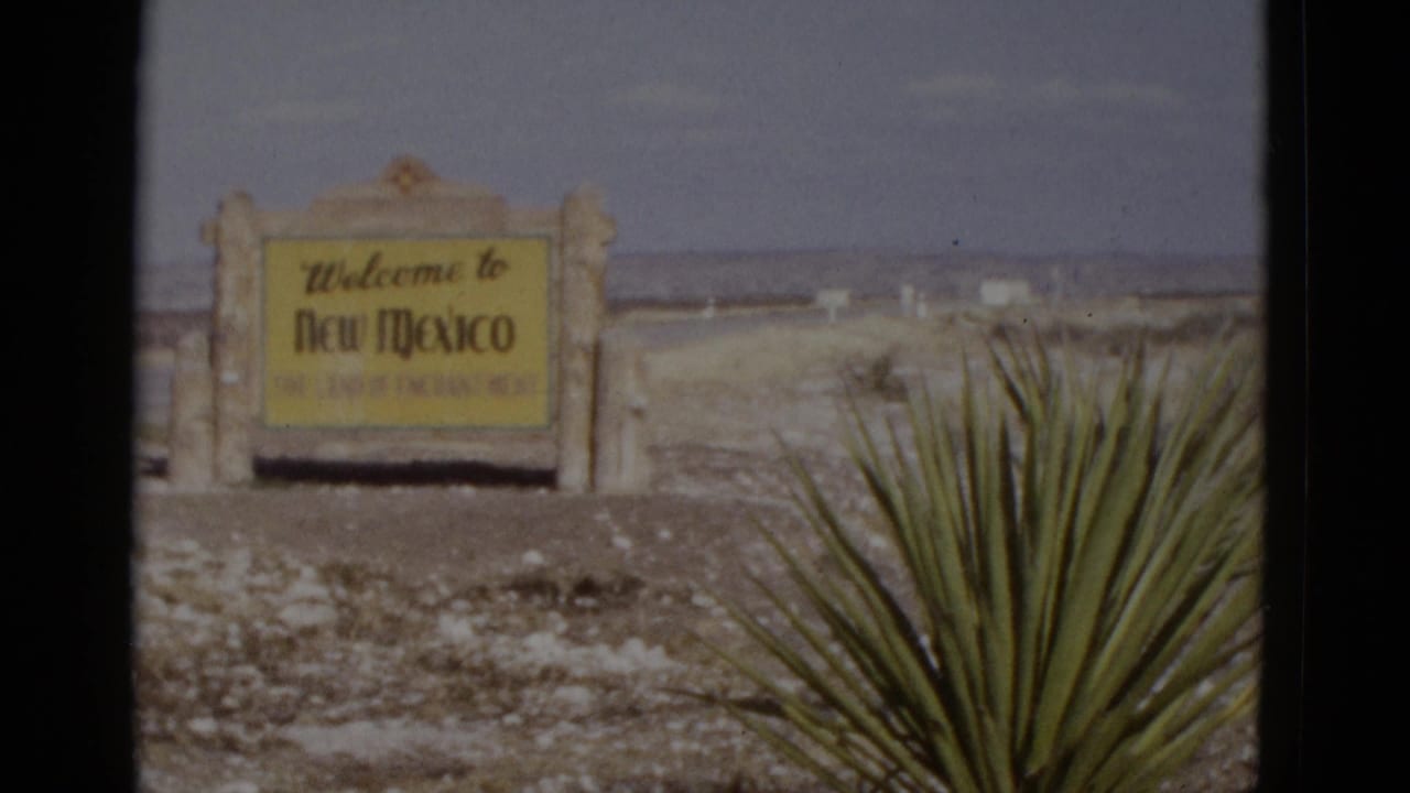 8mm frame from a 1952 Southwest road trip: New Mexico state-line welcome sign on stone pillars, yucca plant foreground, open desert stretching to the horizon.