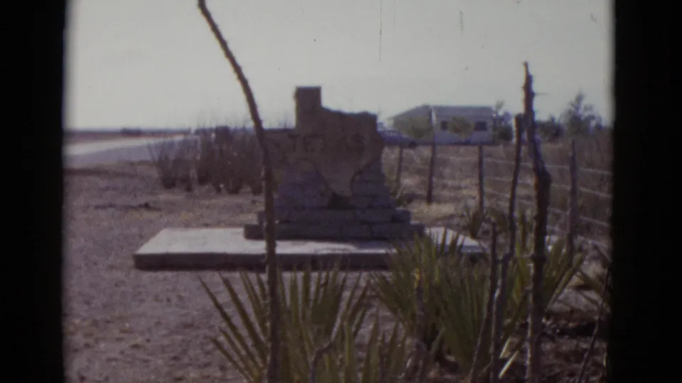 8mm frame of an unidentified stone roadside marker on a concrete platform in Southwest desert terrain, c. 1952; subject and state affiliation unclear from this angle.