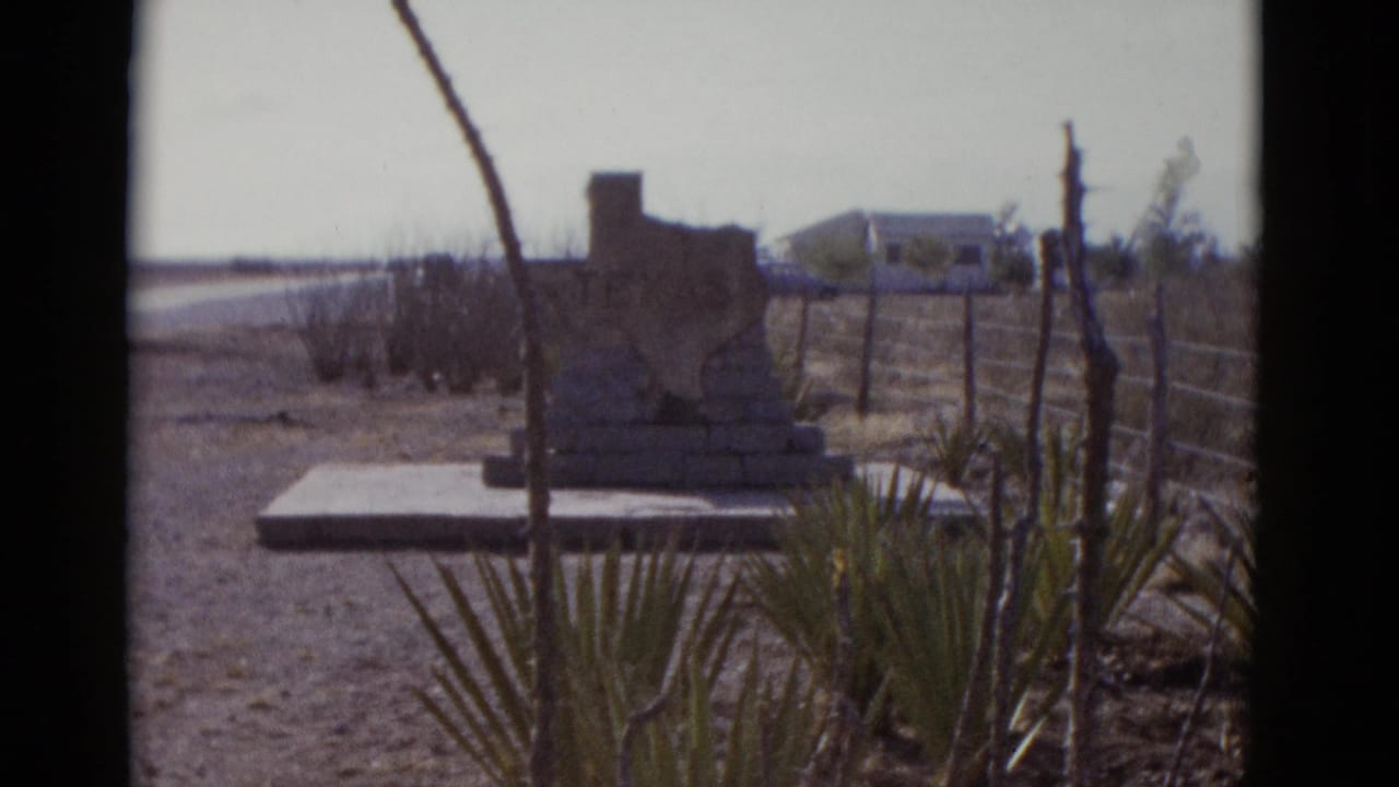 8mm film frame, circa 1952, showing a Texas-shaped roadside stone monument in an arid Southwest landscape with yucca plants and a distant vehicle.