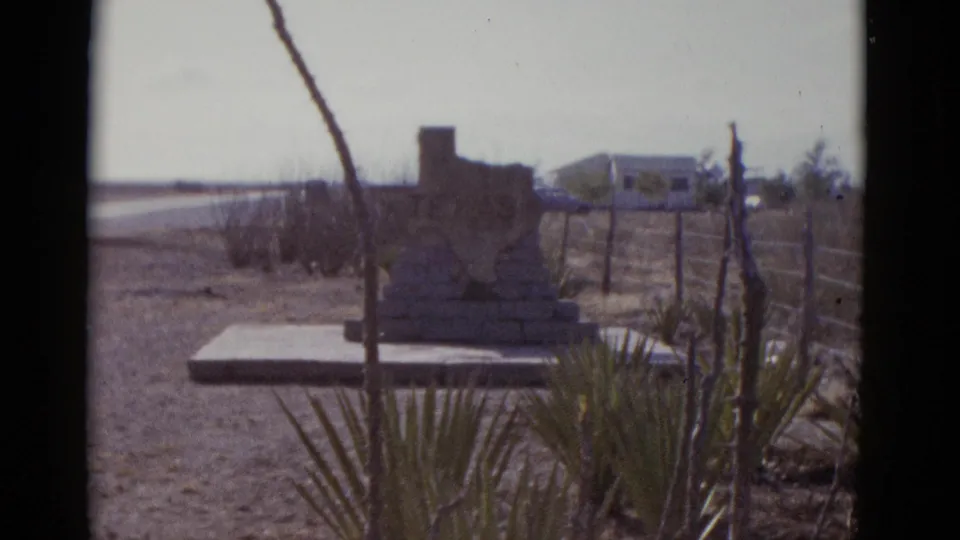 8mm film frame, circa 1952; camera has moved slightly closer to the Texas-shaped roadside monument, framing it between yucca plants and bare dried stalks.