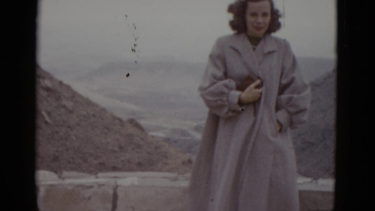 Young woman in long pale coat poses at desert overlook; film dust specks visible in upper right of frame.