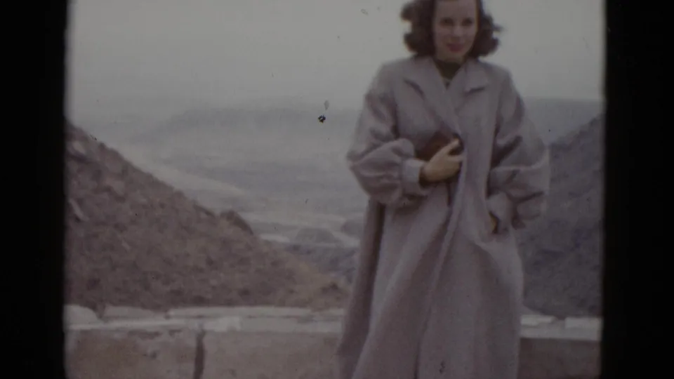 Young woman in full-length pale coat at Utah desert overlook, 1952; broader coat silhouette visible in lower framing, bare hills and flat sky behind.