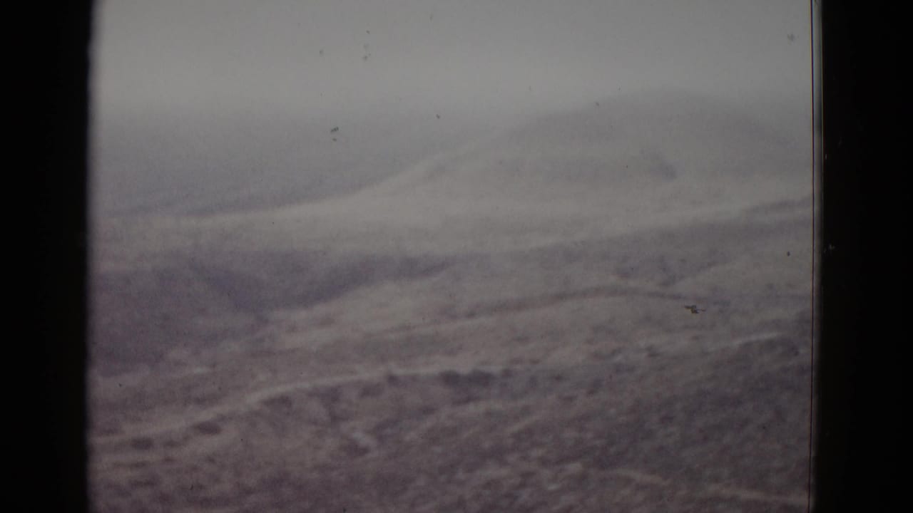 Grainy 8mm view of layered arid mounds receding toward a pale hazy horizon.