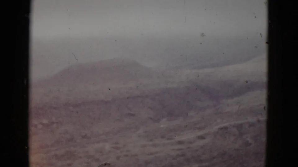 8mm home-movie frame, likely Utah, 1952 — isolated rounded earth mound rising from dry scrubland under an overcast sky.