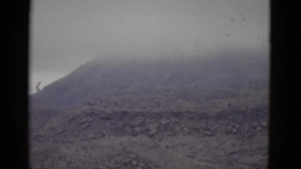 Bare conical mountain against an overcast sky, likely Utah, from a 1952 8mm home movie; a small dark figure may be visible near the ridgeline.