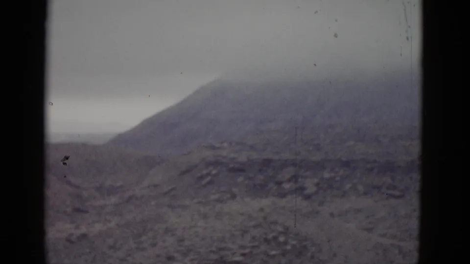 Wide view of a barren mountain and arid slopes, likely Utah, from a 1952 8mm road-trip home movie; film shows heavy blue-gray color fade and dust specks.