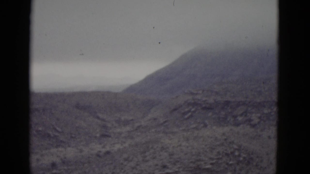 Arid rocky hillside consistent with Utah desert terrain, shot on 8mm film circa 1952, under a flat overcast grey sky.