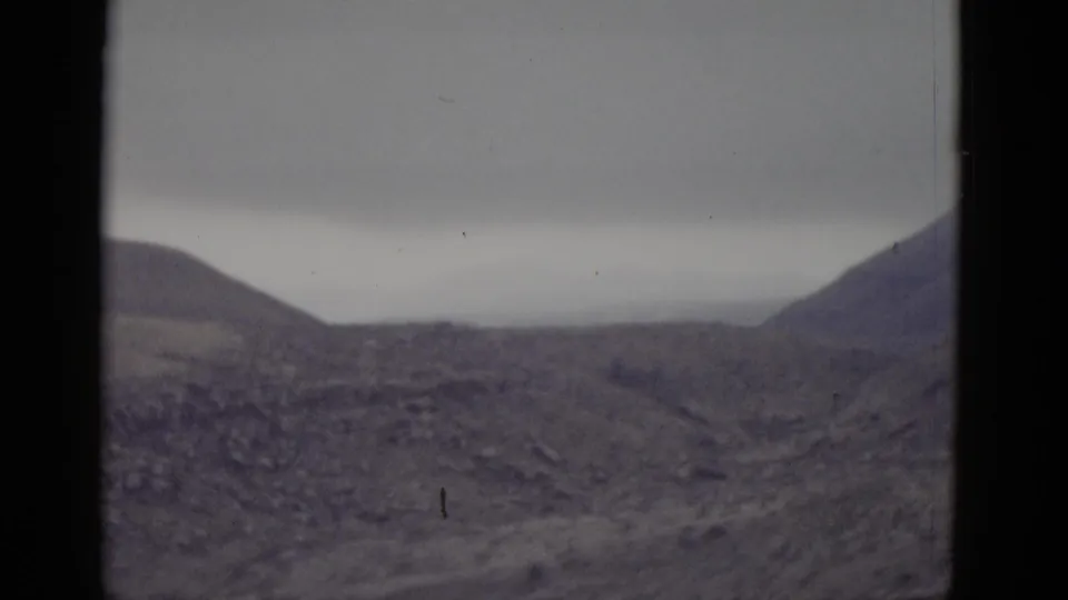 Broad arid landscape with a low desert hill under flat overcast sky, consistent with Utah terrain, shot on 8mm film circa 1952.