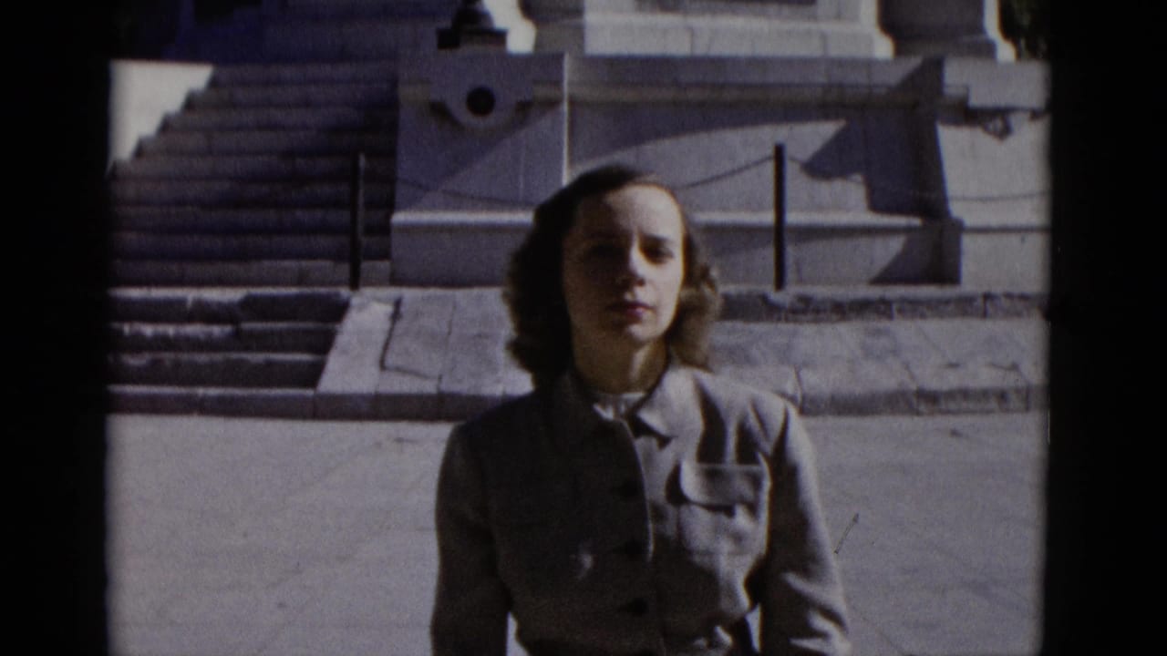 Young woman in a grey jacket stands before the wide stone steps of a large white monument, looking toward the camera.