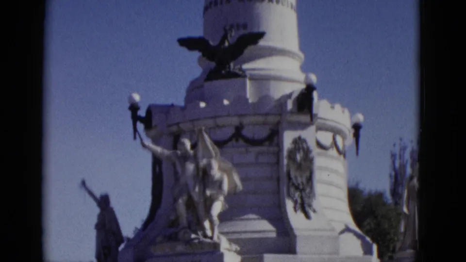 8mm frame from 1952: upper monument column with dark spread-wing eagle emblem, crenellated battlements, lamp fixtures, and sculptural figures visible below.