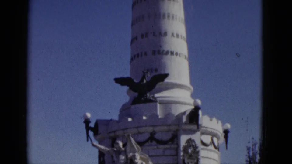 Low-angle 1952 8mm home-movie shot of a tall white commemorative column with eagle sculpture and Spanish inscriptions, attributed to Utah, USA.