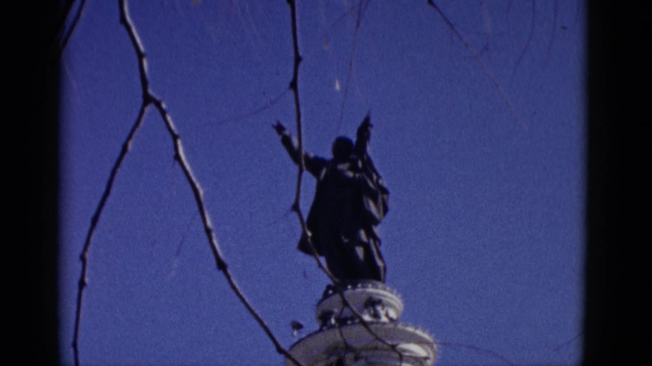 Film-damaged 8mm frame showing a silhouetted statue or roadside monument against blue sky, circa 1952, from a travel reel.