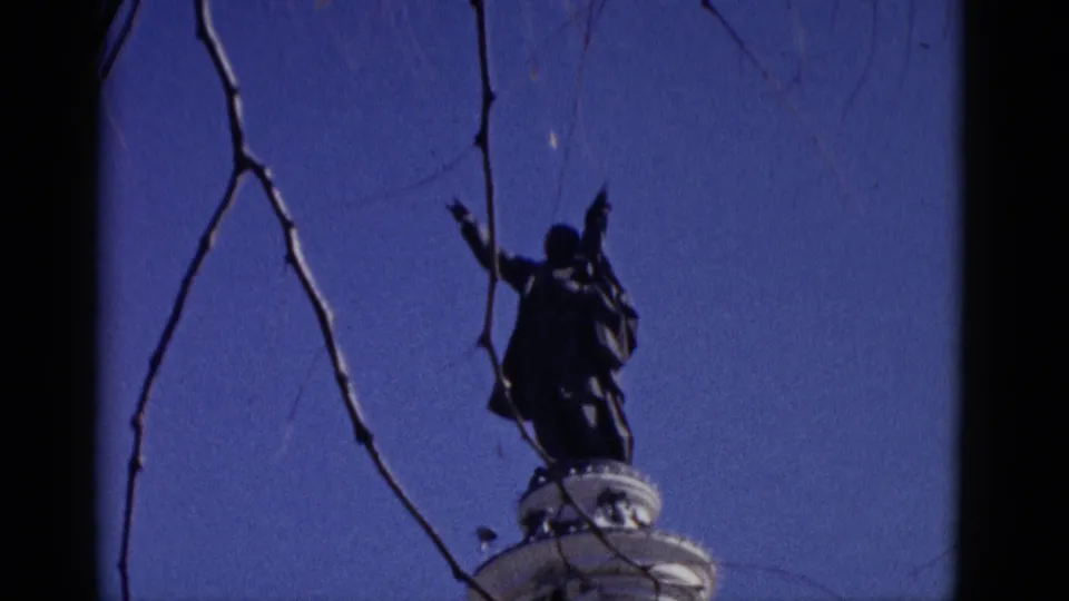 Film-damaged 8mm frame showing a silhouetted statue or roadside monument against blue sky, circa 1952, from a travel reel.