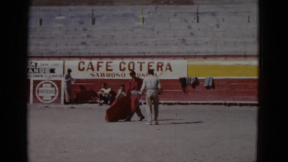 Matador practicing with a red muleta on the sandy floor of what appears to be a 1952 Baja California bullring; commercial signage on arena wall.
