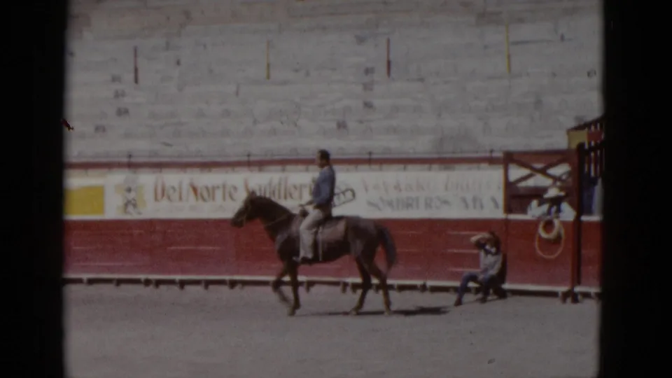 8mm home movie, circa 1952, Baja California, Mexico: horseman in blue jacket at slow trot, arena advertising and seated spectator clearly visible.