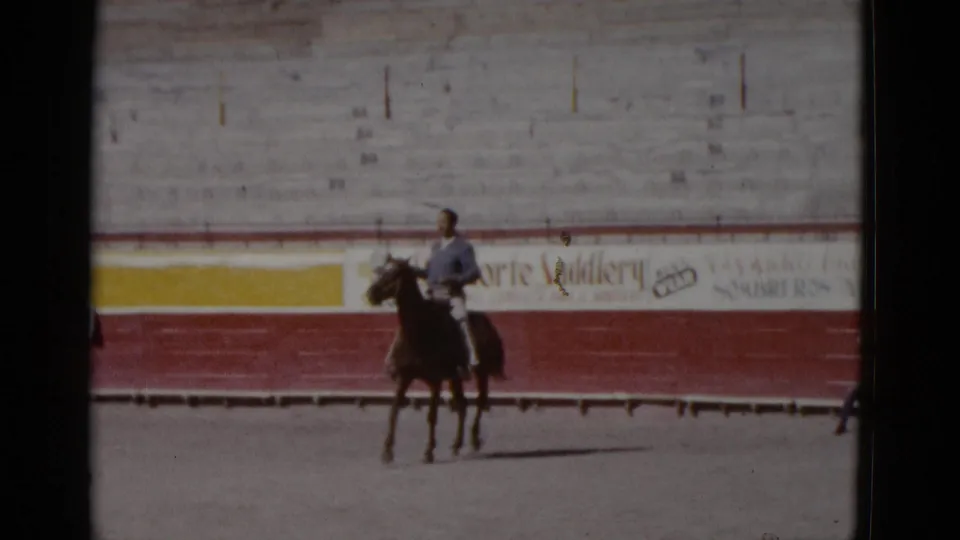 8mm color film, circa 1952, Baja California, Mexico: rider and horse in mid-arena, advertising-painted barrier visible, objects near base of wall.